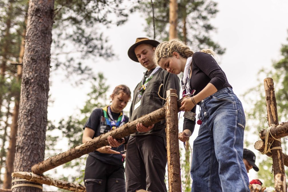 Three scouts building something from small tree trunks.